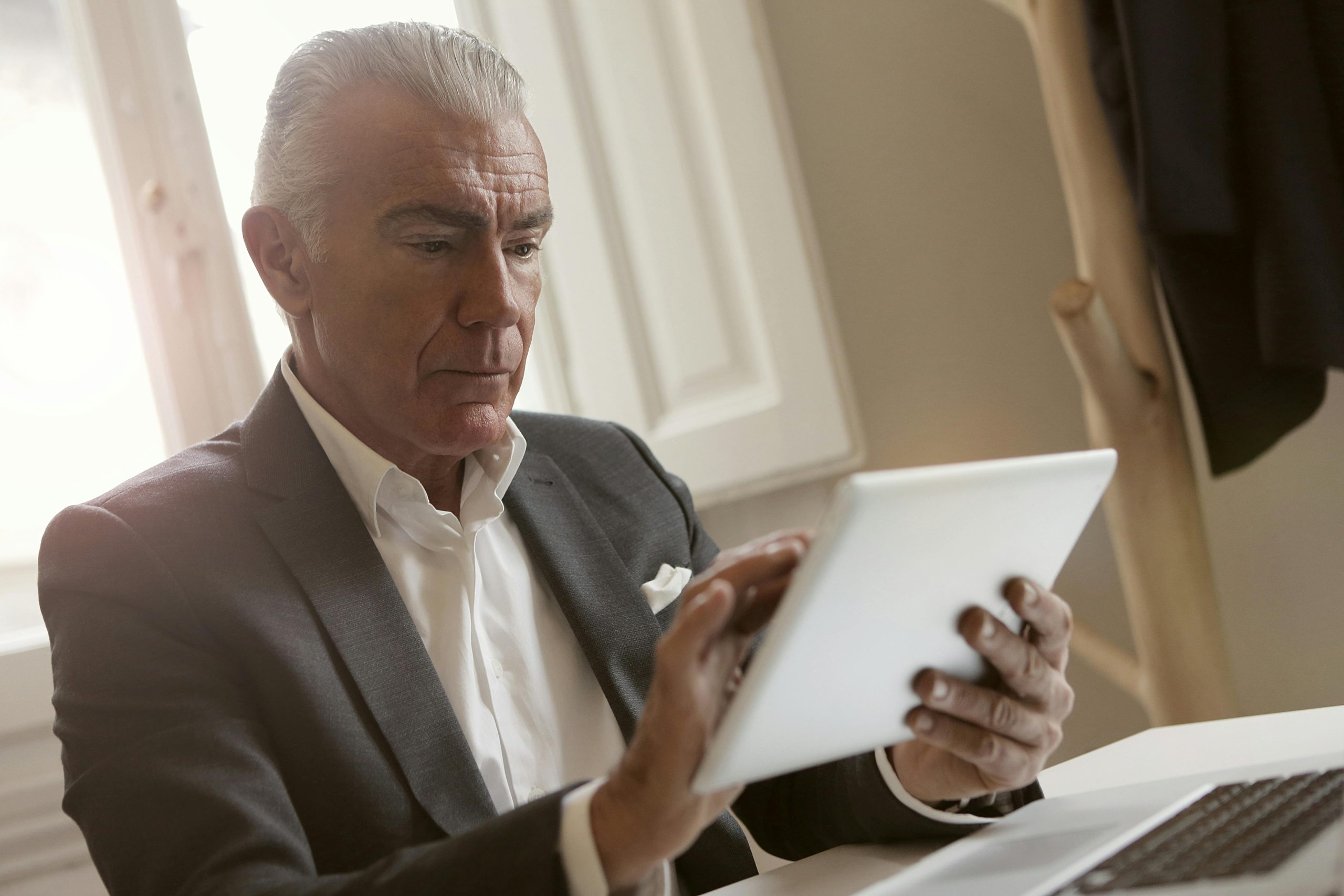 Elderly businessman focused on using a tablet for work in an office setting.